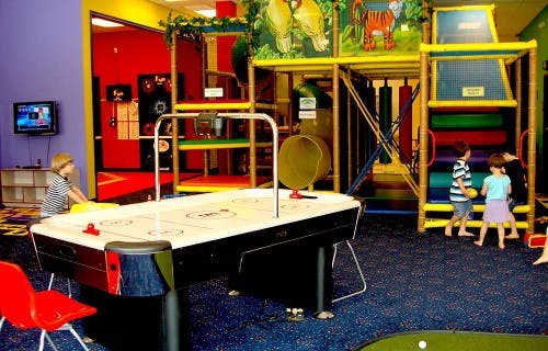 Children playing air hockey and on an indoor playground structure