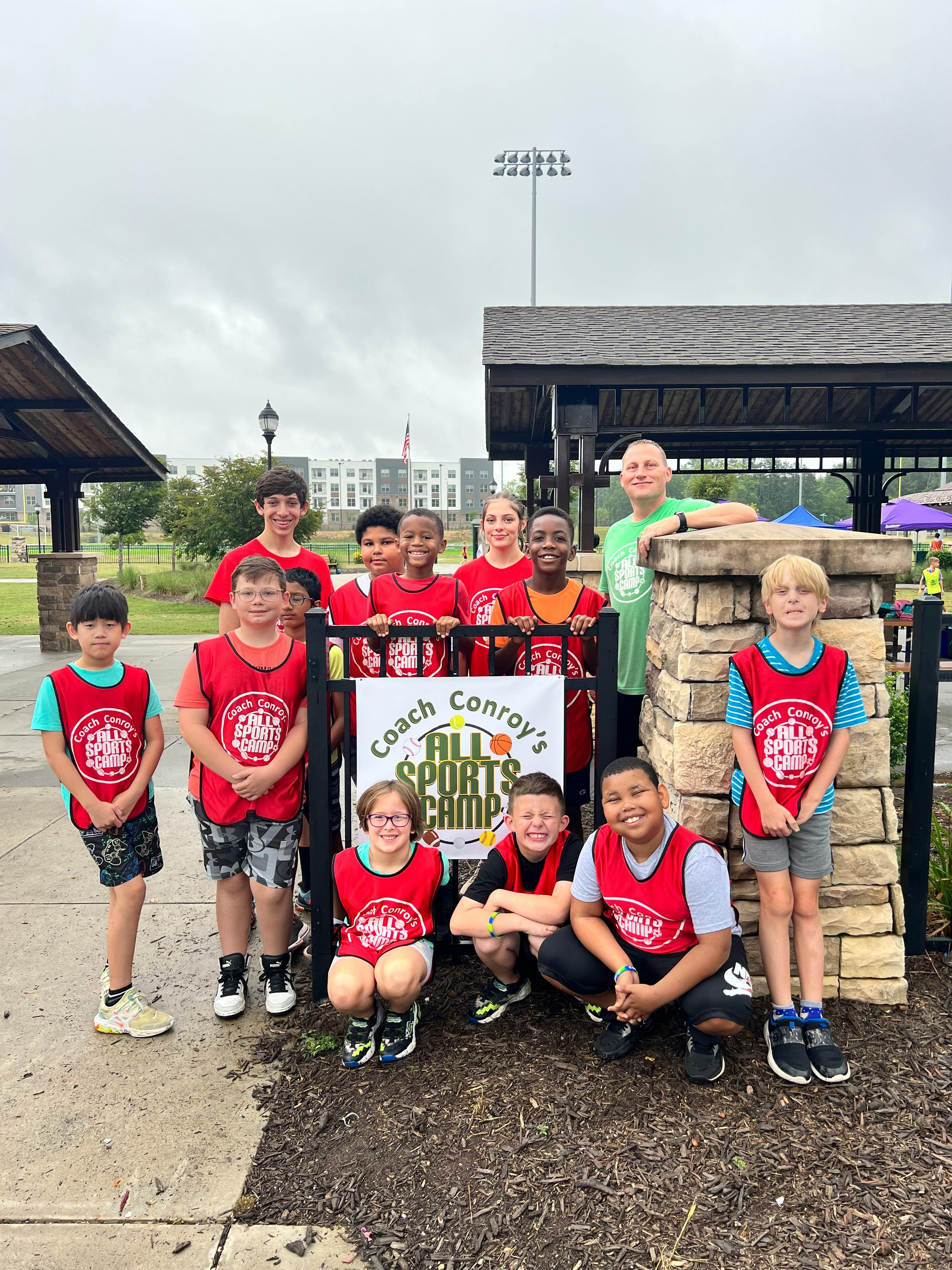 Group of children and adults posing with a "Coach Conroy's All Sports Camp" banner