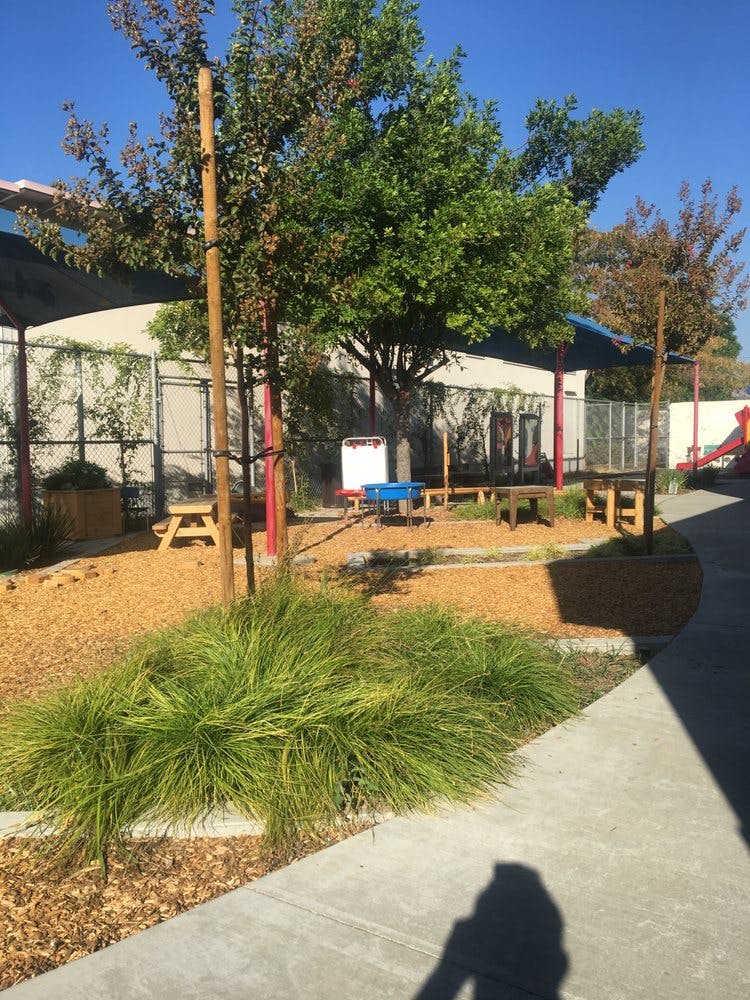 Outdoor play area with wood chips, trees, and small picnic tables