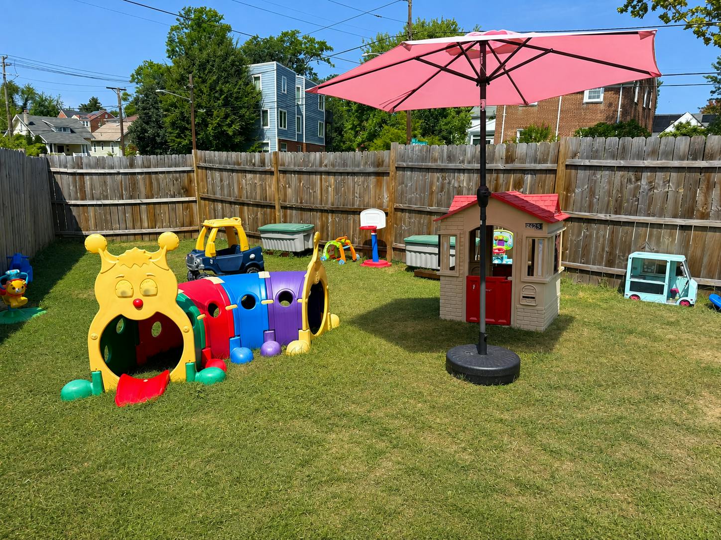 Colorful plastic play equipment on a grassy backyard lawn with a pink umbrella