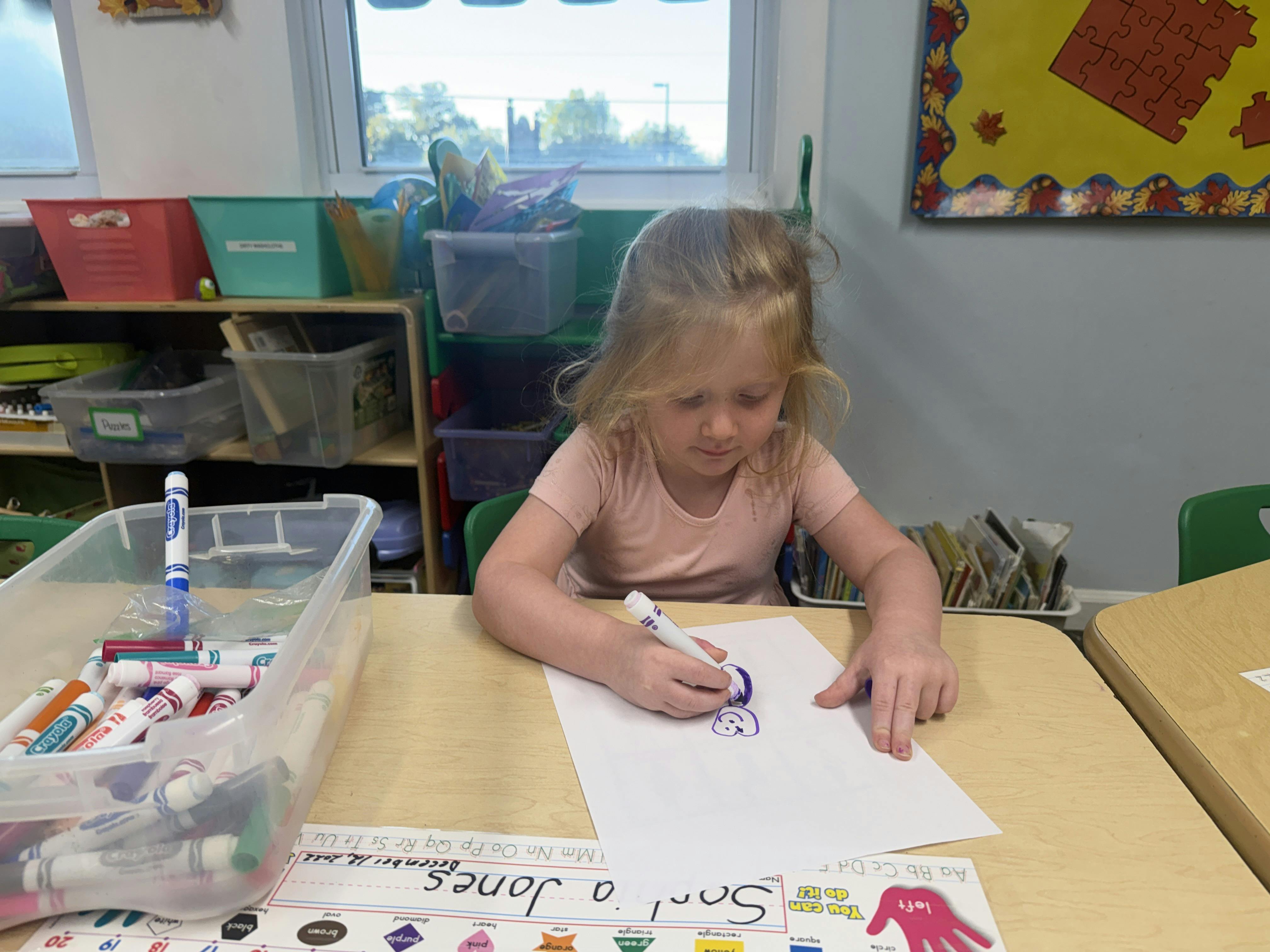 Child drawing with a marker on a sheet of paper at a desk in a classroom