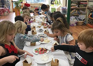 Children decorating gingerbread houses at a long table