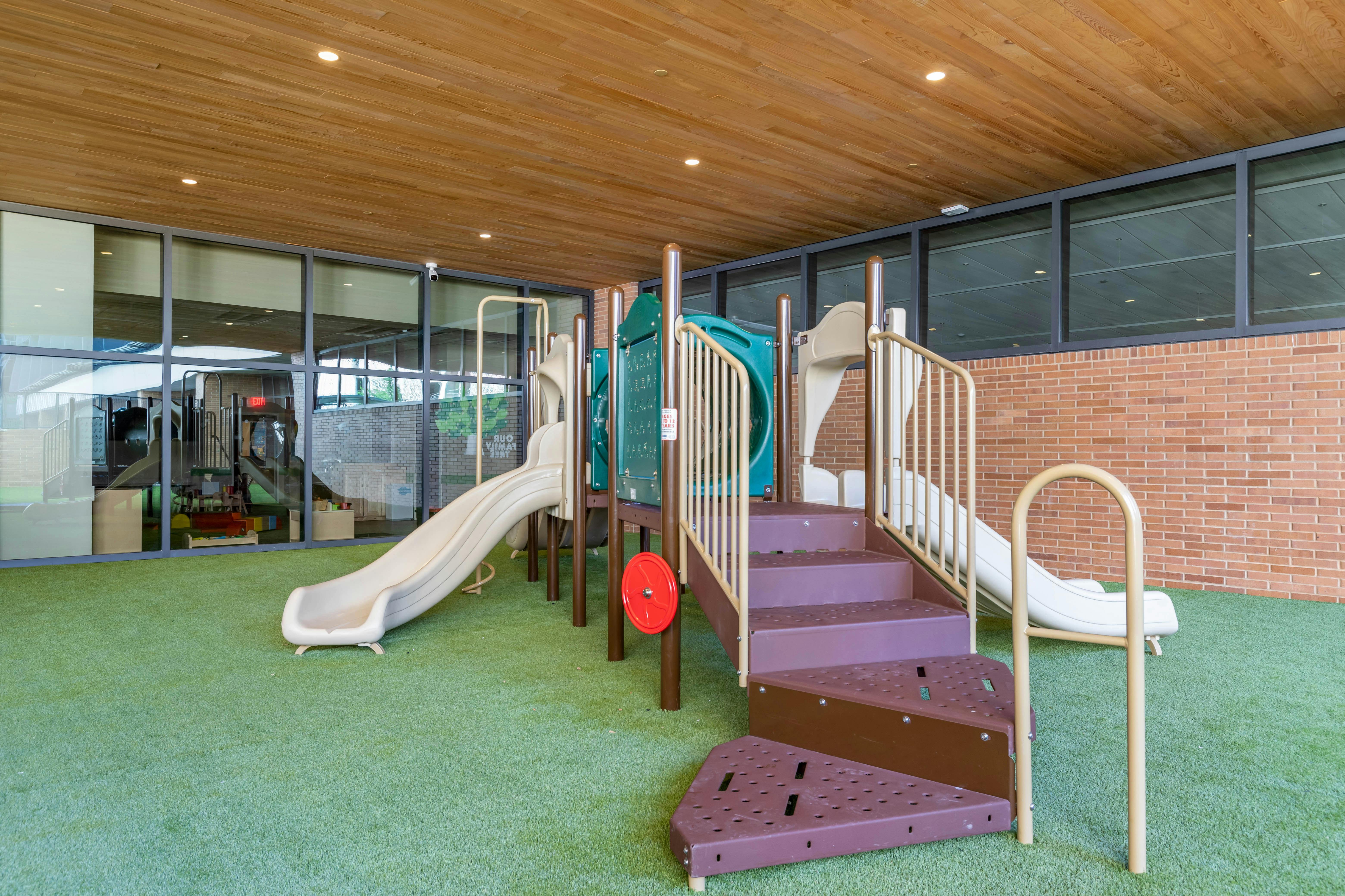 Indoor playground with multiple slides, stairs, and play structures on artificial turf
