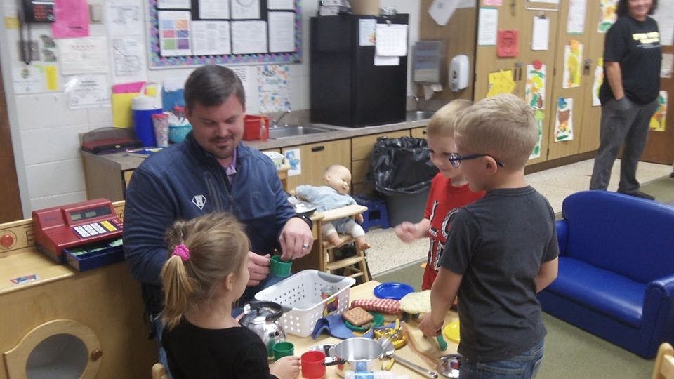 Adult and three children interacting around a table in a classroom
