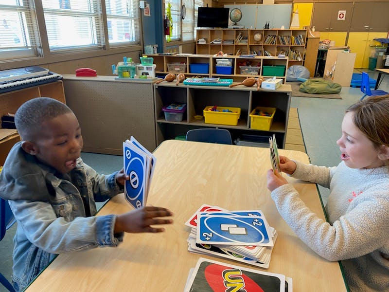 Two children playing cards at a table in a classroom