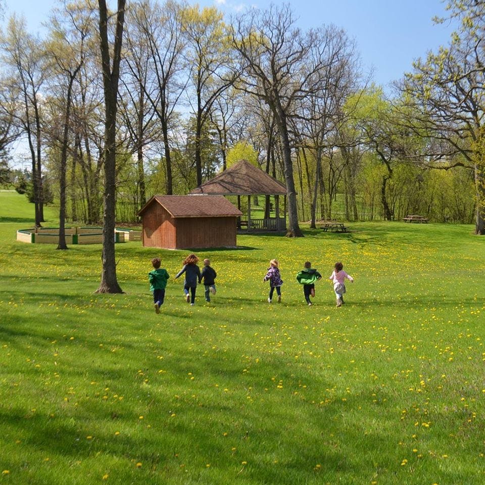 Children running across a grassy field with trees and a small building in the background