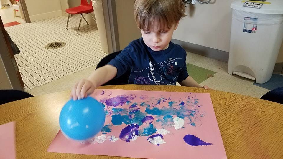 Child using a balloon to paint on paper
