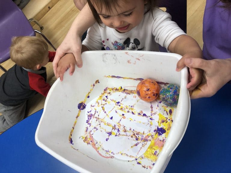 Child and adult holding a bin with painted paper and balls