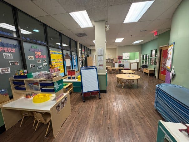 Empty classroom with small tables and chairs, and art supplies on shelves