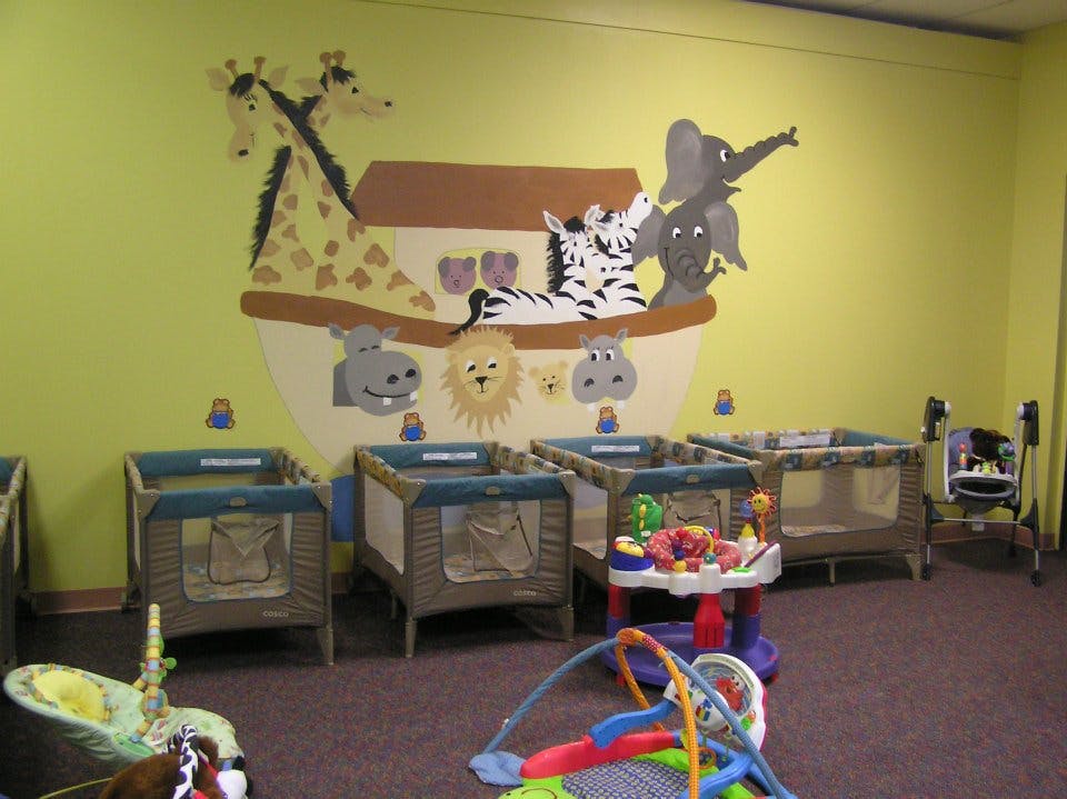 Nursery room with multiple cribs and a wall mural of animals in an ark