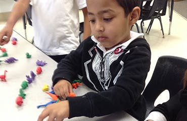 Child playing with colorful clay figures at a table