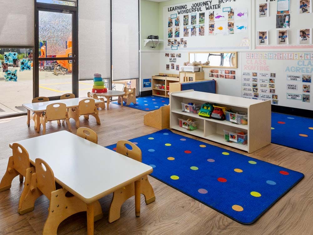 Classroom with small tables, chairs, colorful rugs, and learning materials