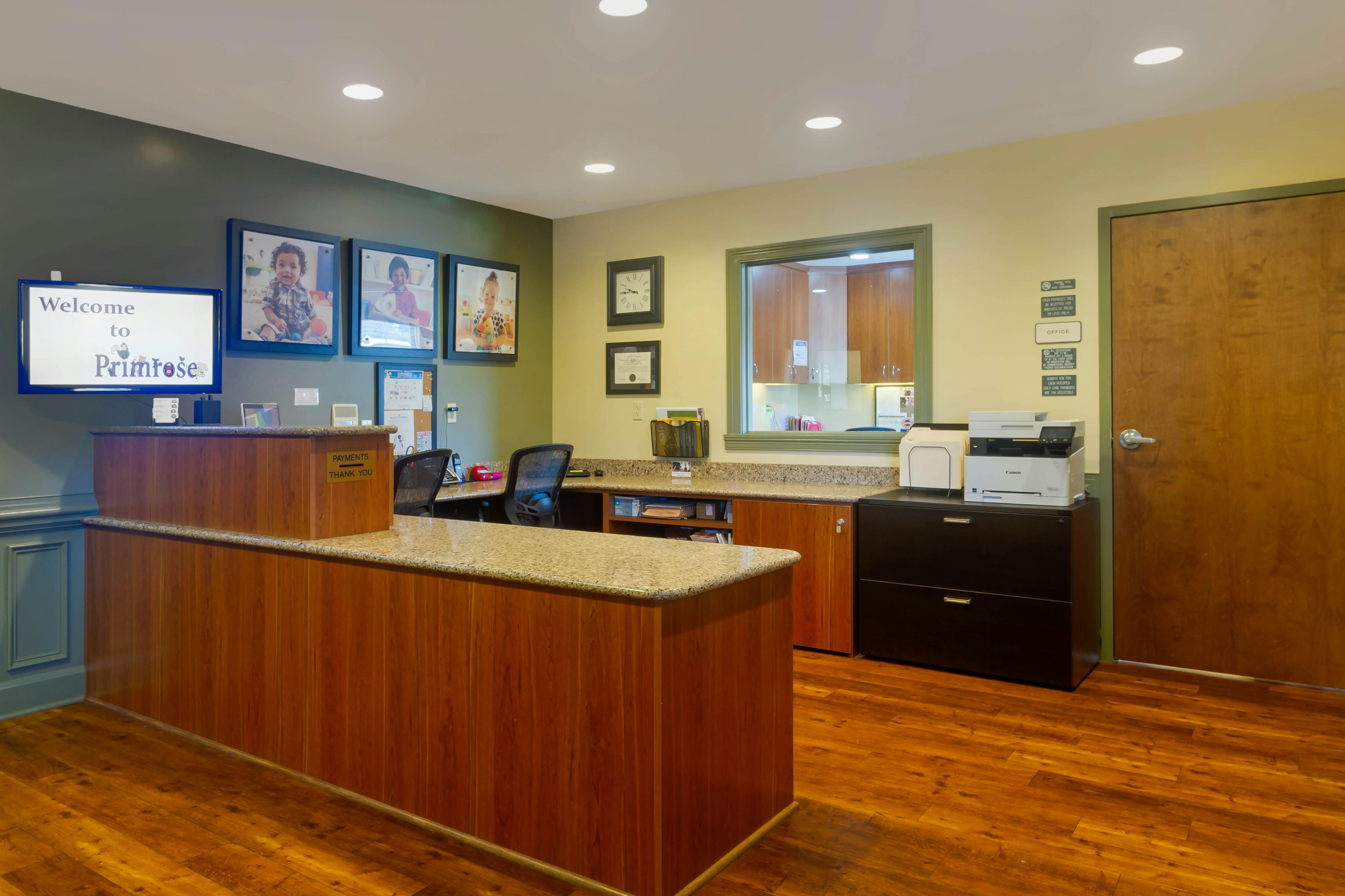 Reception desk with 'Welcome to Primrose' on a screen, and child portraits on the wall