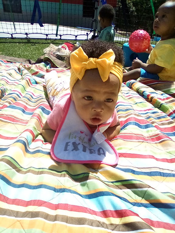 Child with a yellow bow headband and bib on a striped blanket
