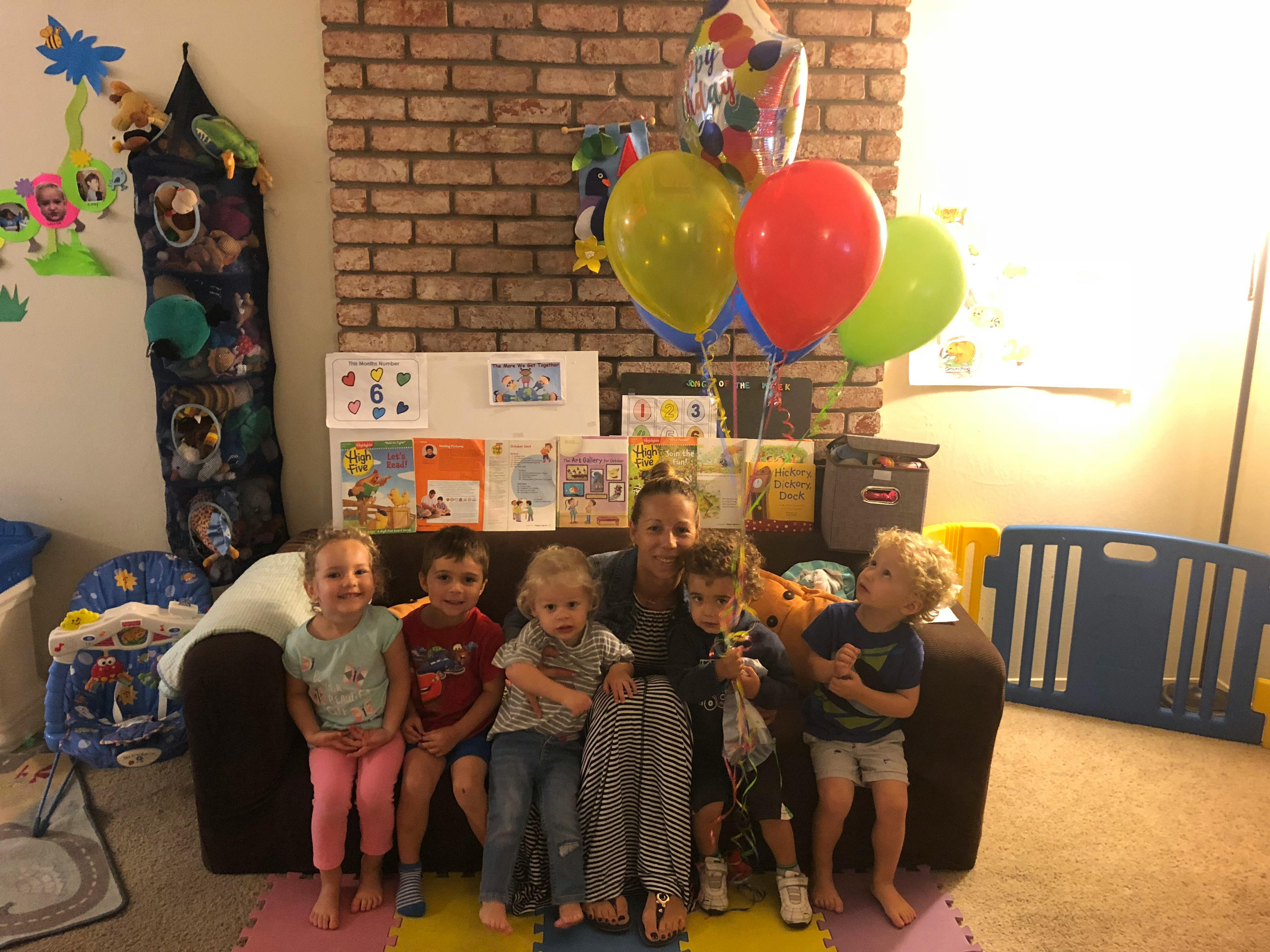 Adult and multiple children sitting on a couch with balloons