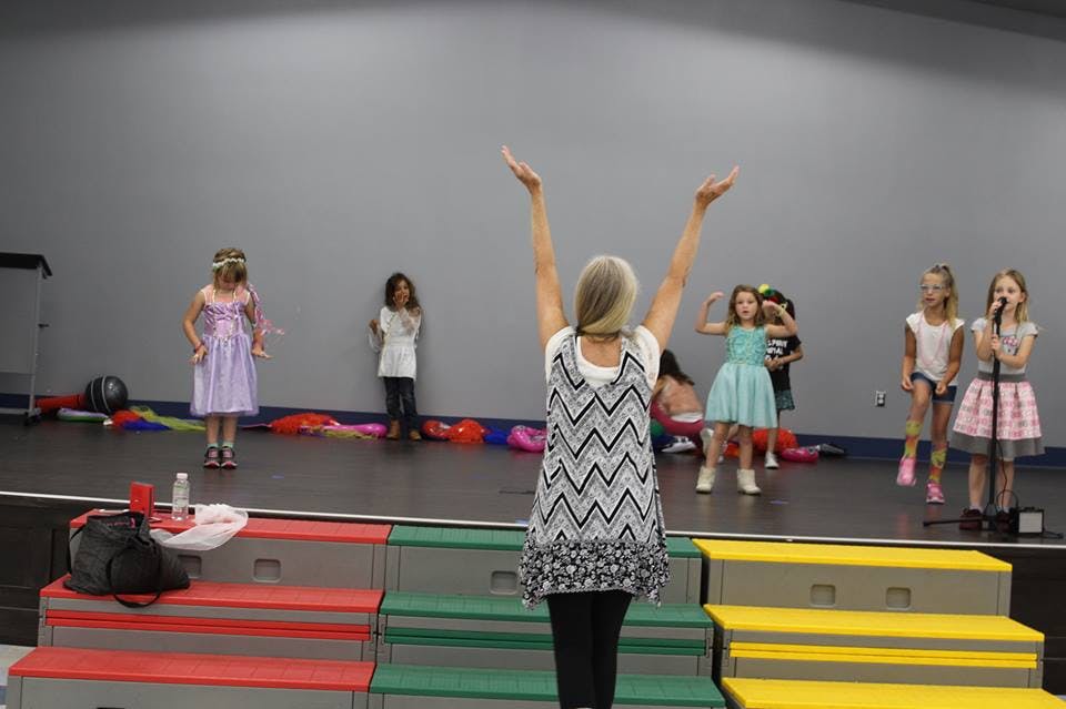 Adult with arms raised leading children on a stage