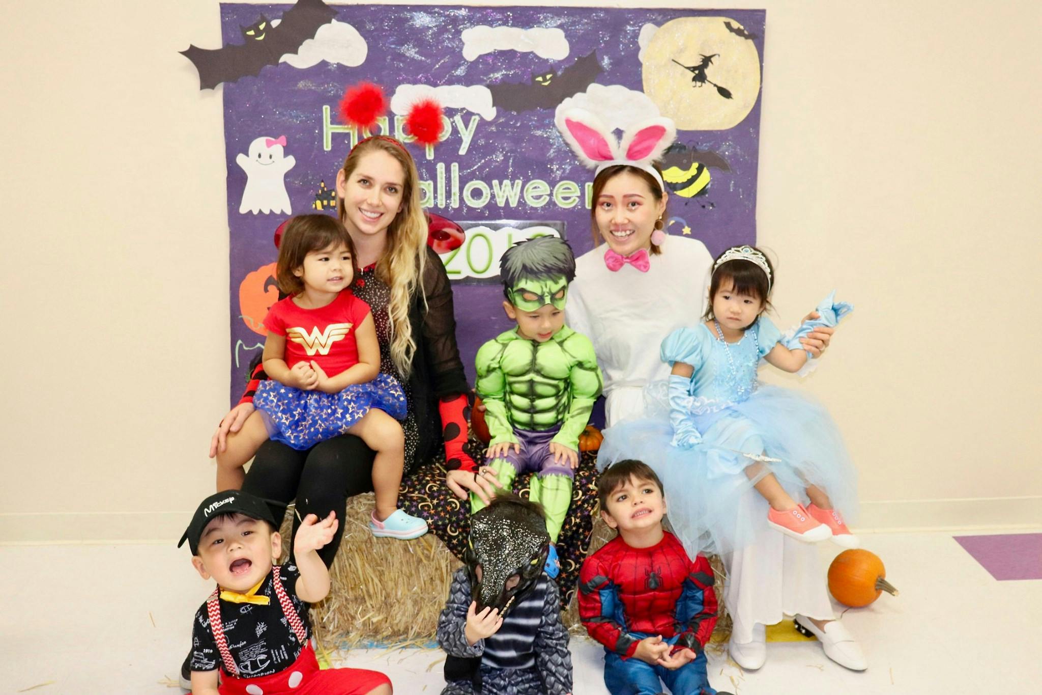 Two people and five children in Halloween costumes in front of a Halloween sign