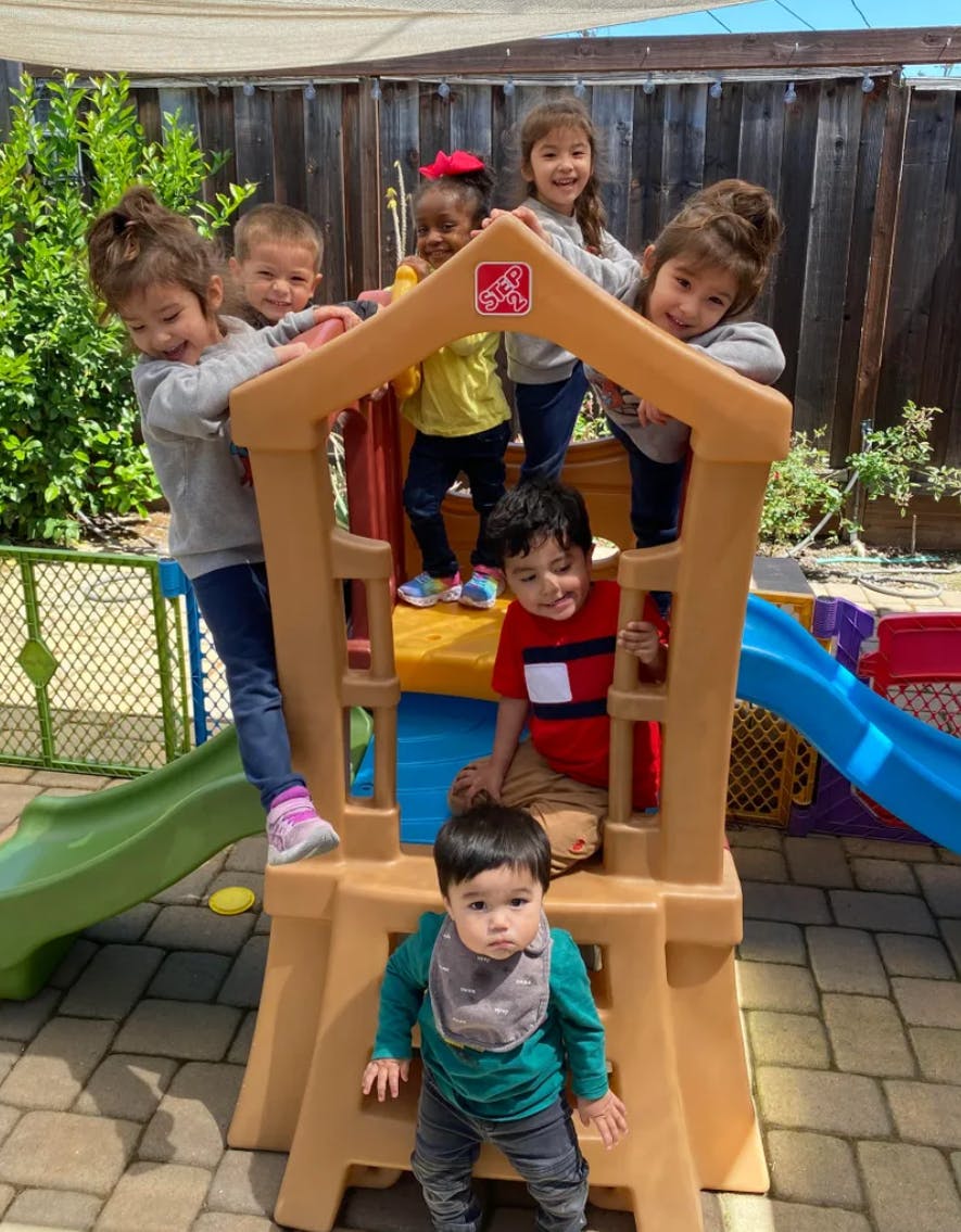 Children playing on and around a plastic play structure outdoors