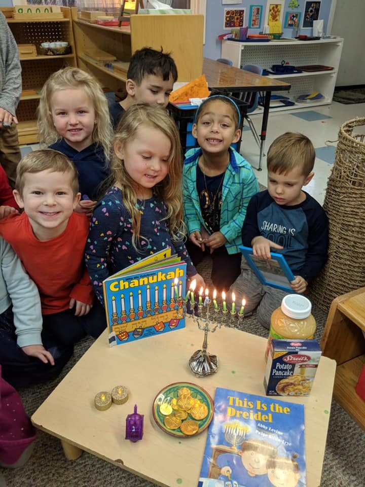 Children gathered around a table with a menorah, books, and Hanukkah items