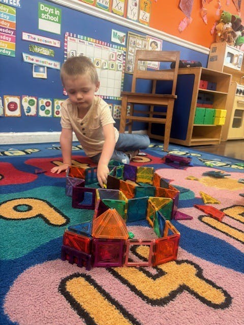 Child building with colorful magnetic tiles on a rug in a classroom