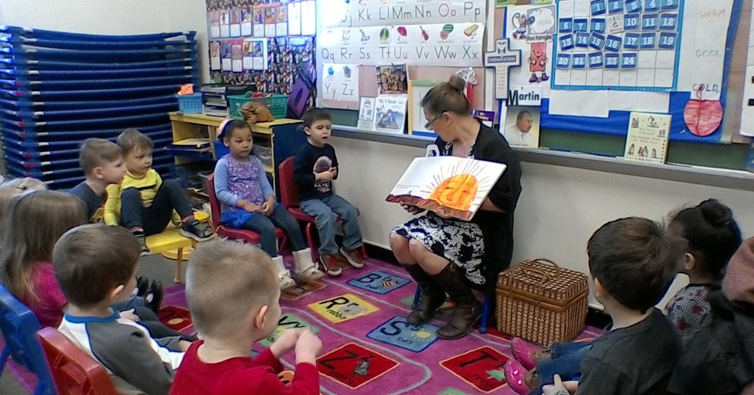 Person reading a book to children in a classroom