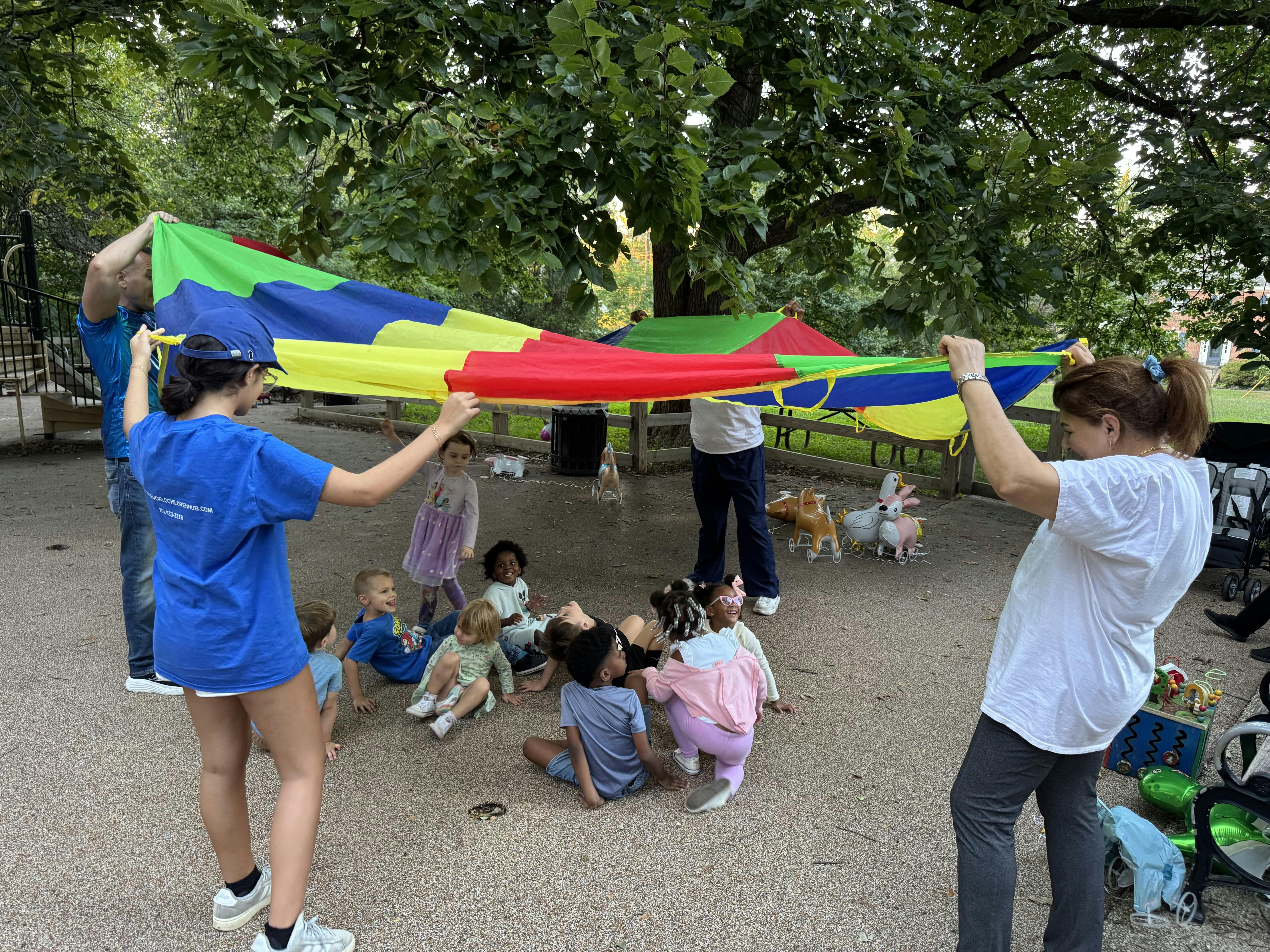 People holding a colorful parachute over children sitting on the ground