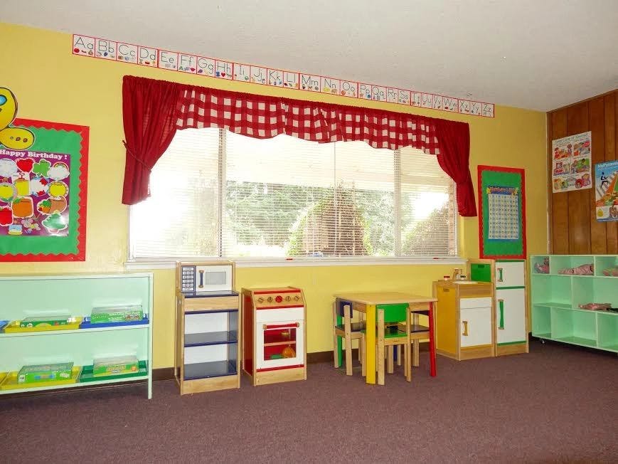 Classroom with small tables and chairs, toy kitchen, and shelves