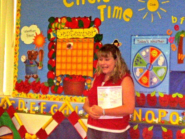 Person holding papers in front of a classroom bulletin board