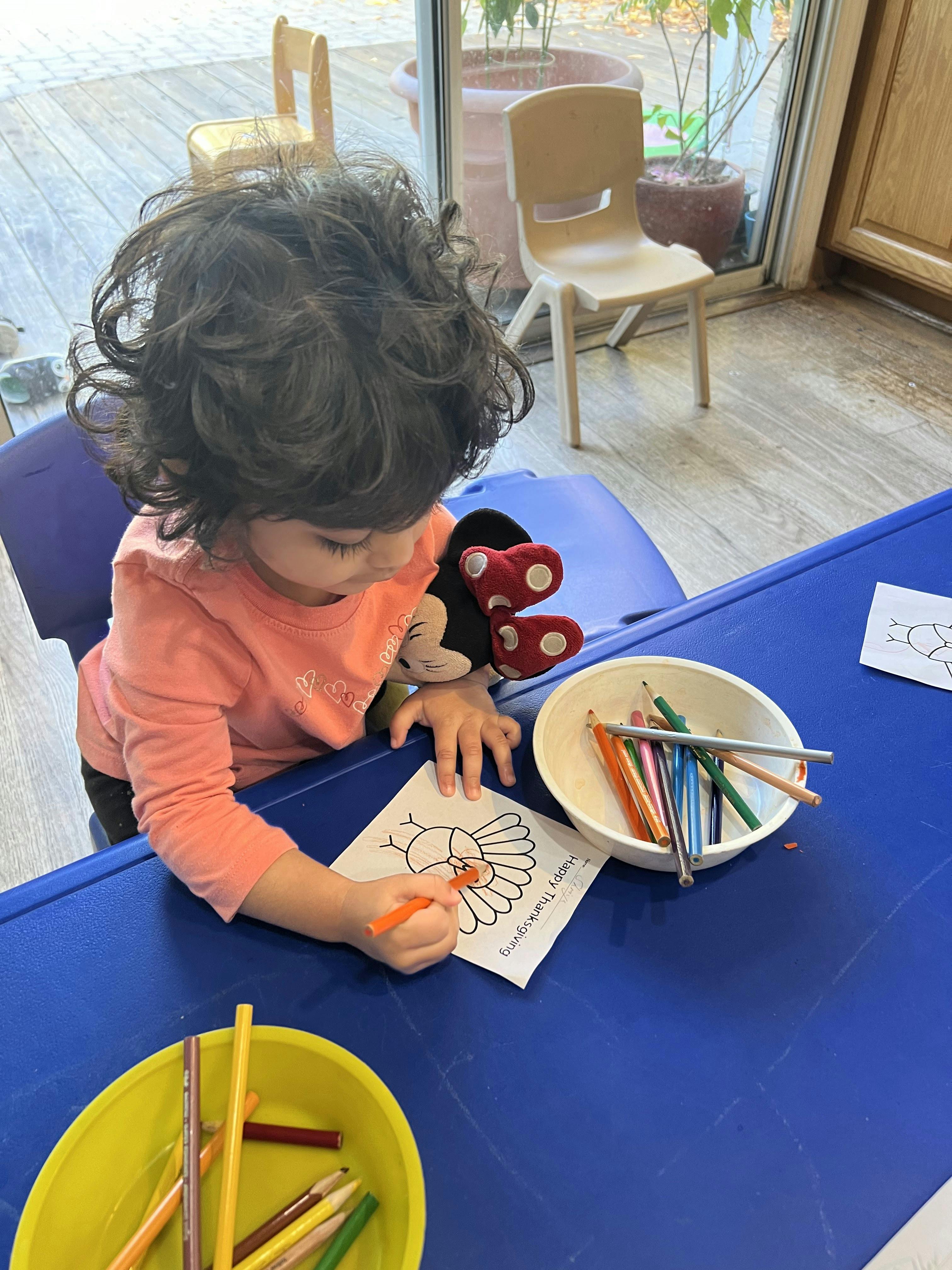 Child coloring a turkey picture at a blue table in a classroom