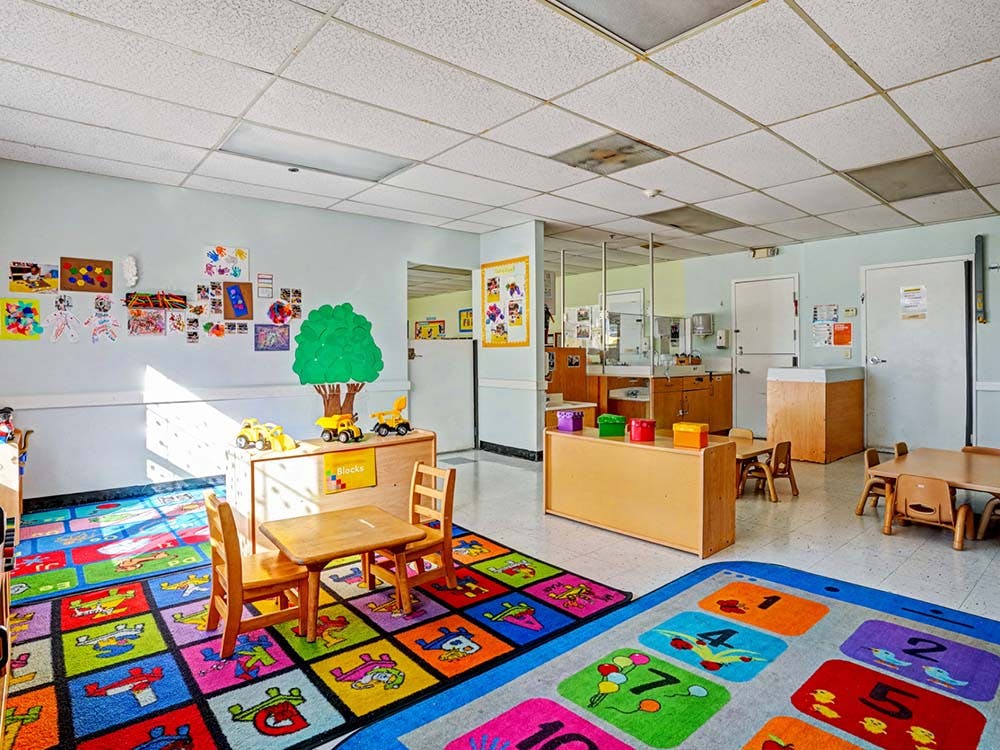 Colorful classroom with child-sized tables and chairs, play mats, and artwork on walls