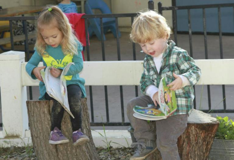 Two children sitting on tree stumps reading books