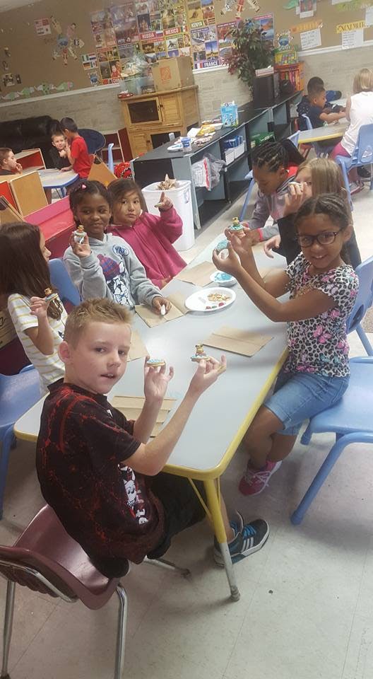 Children at tables holding small crafts in-progress craft items
