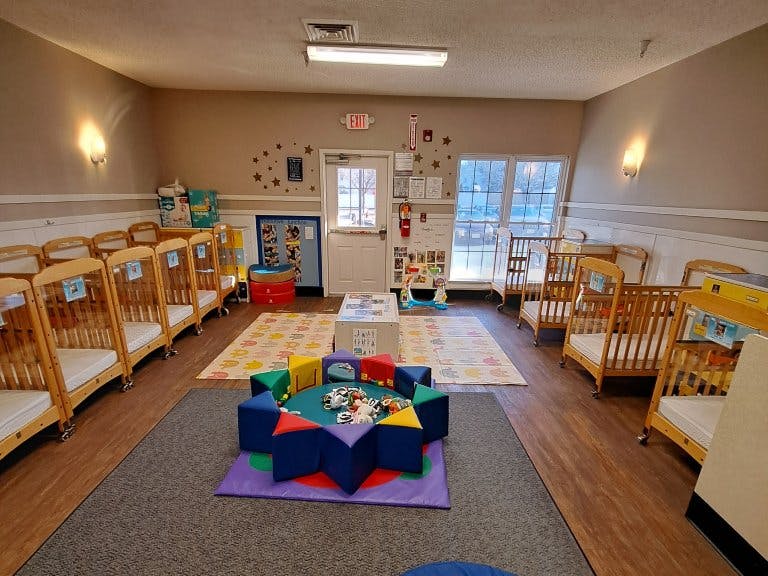 A room with multiple infant cribs lining the walls and play mats on the floor