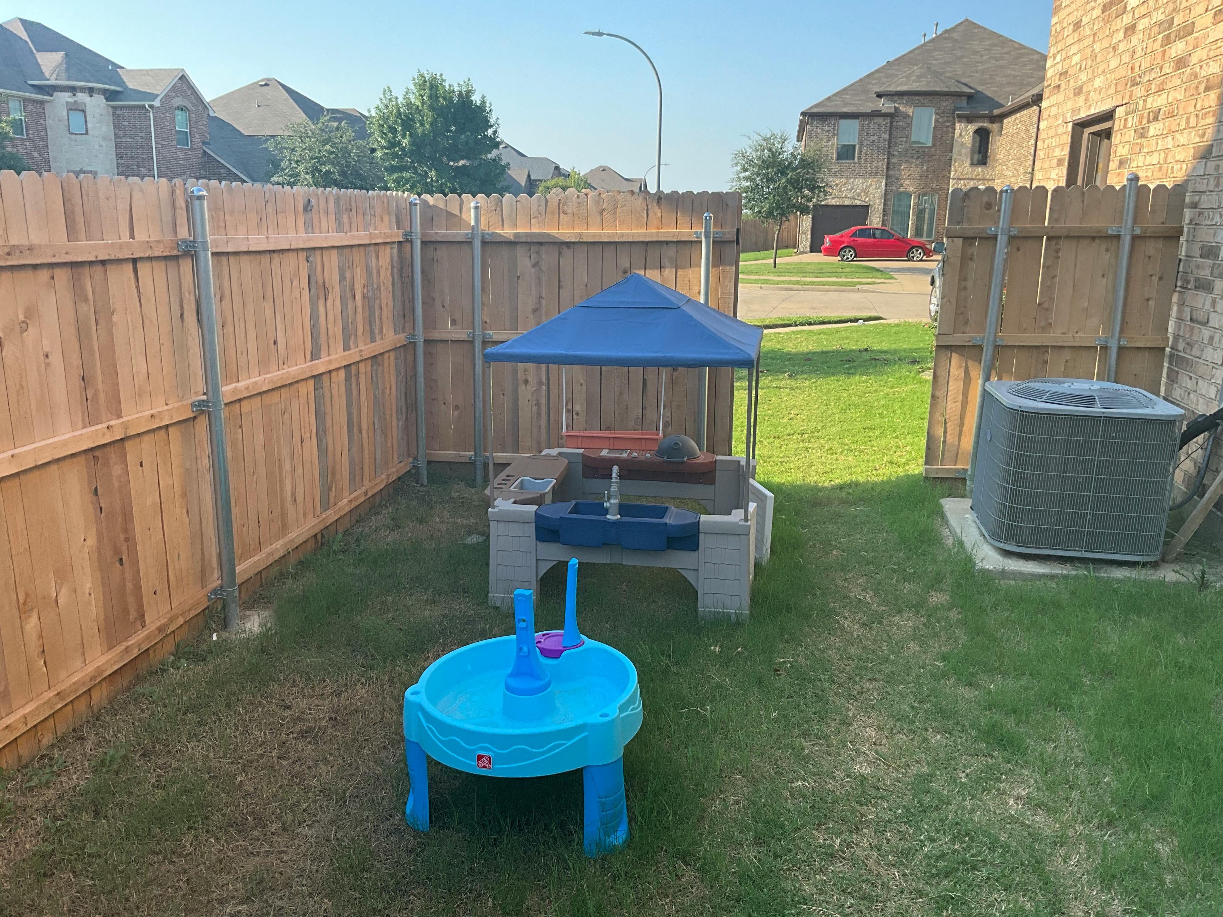 Backyard with a wooden fence, blue play table, and sand and water table