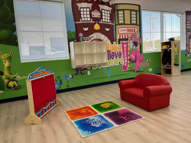 Children's play area with a red couch, colorful floor mat, and puppet stage