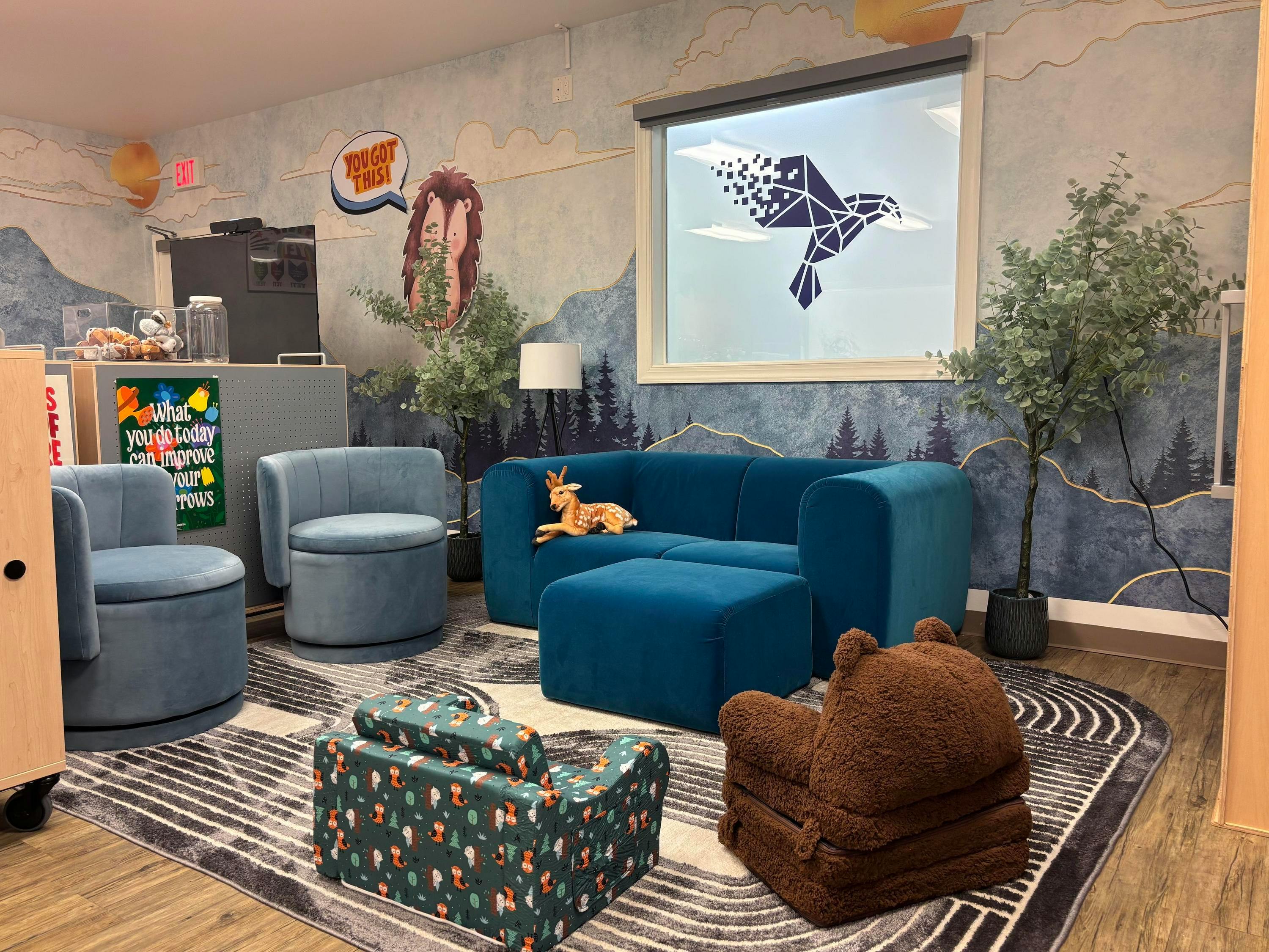 Lounge area with blue couches and chairs, kids' seating, and decorative wall mural