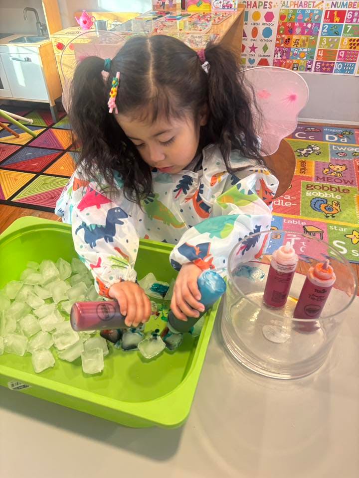 Child in a smock coloring ice cubes in a green tub