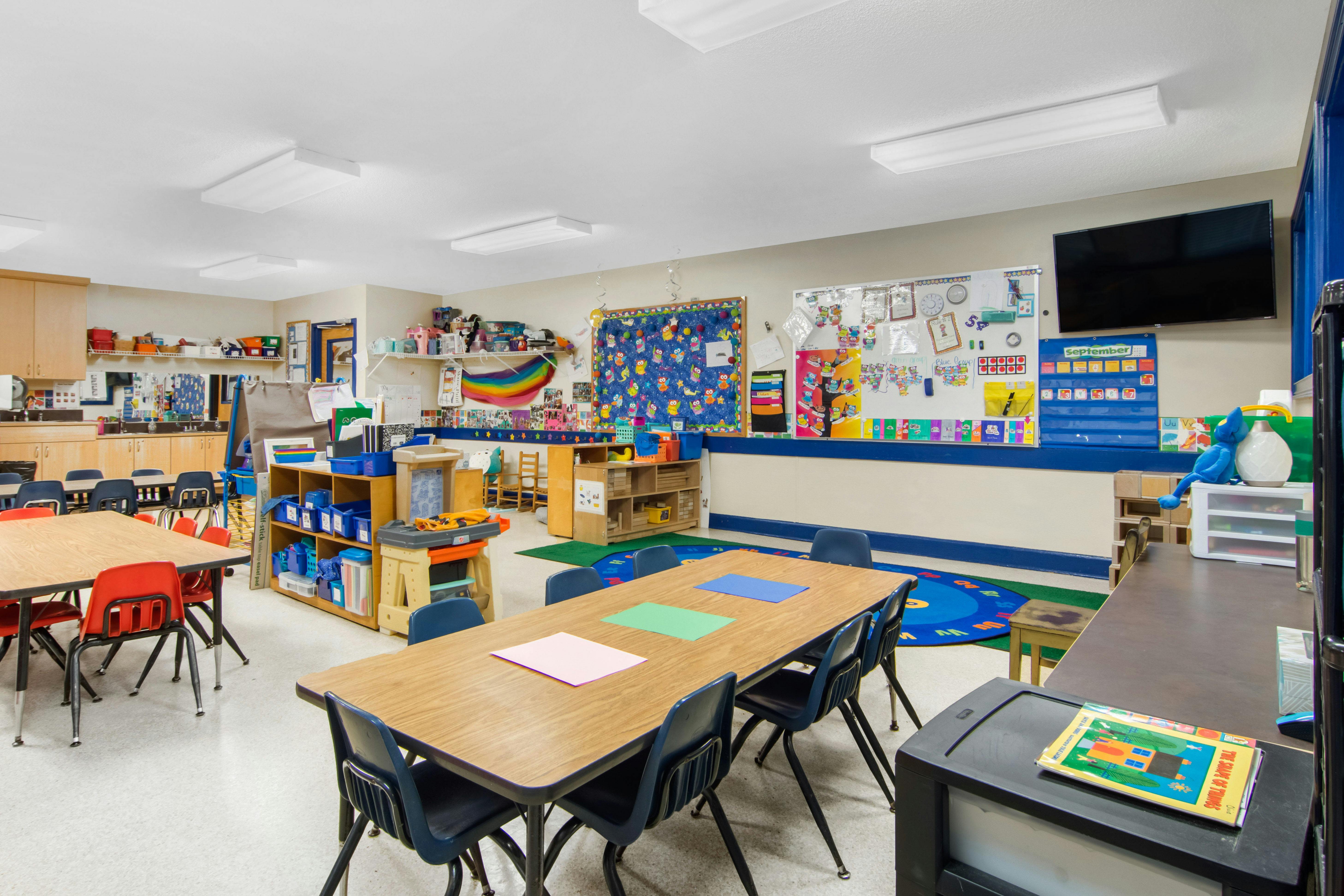 Classroom with tables, chairs, teaching materials, and a wall-mounted TV