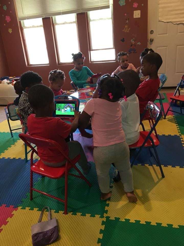 Children gathered around a table with one child looking at a tablet