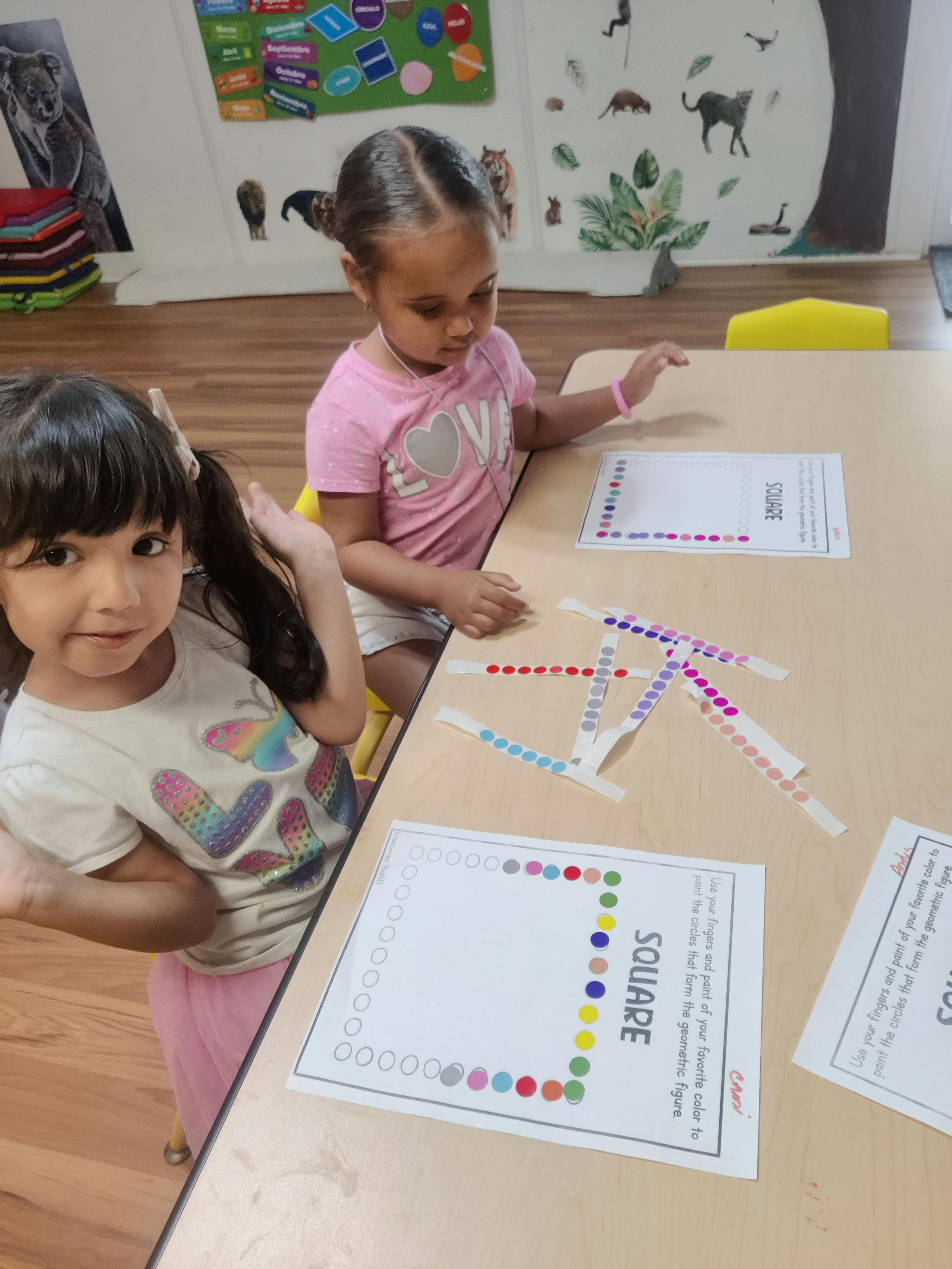 Two children working on square shape worksheets at a table in a classroom