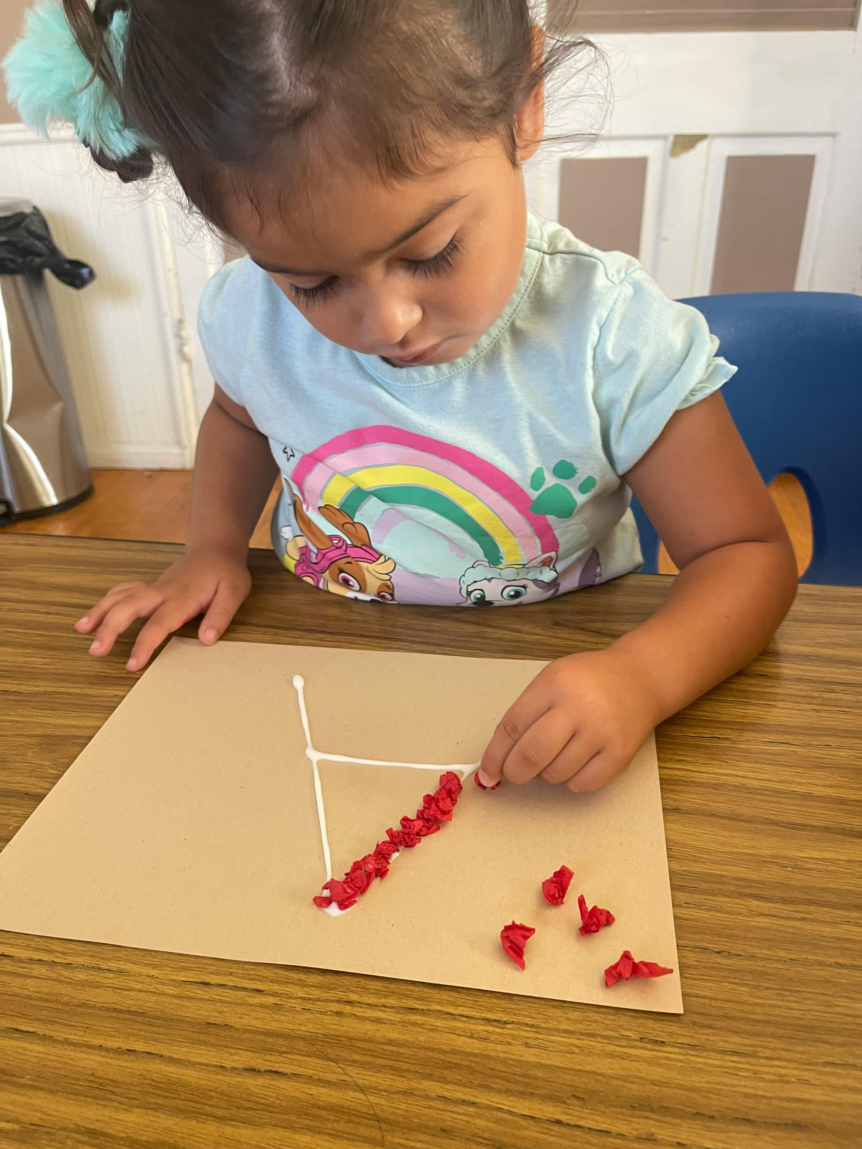 Child creating art with red pieces on a brown paper