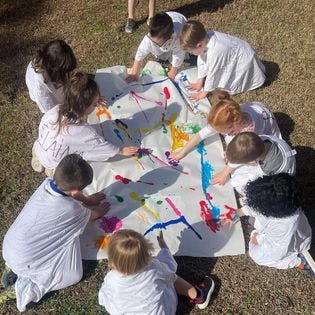Children painting on a large sheet outdoors