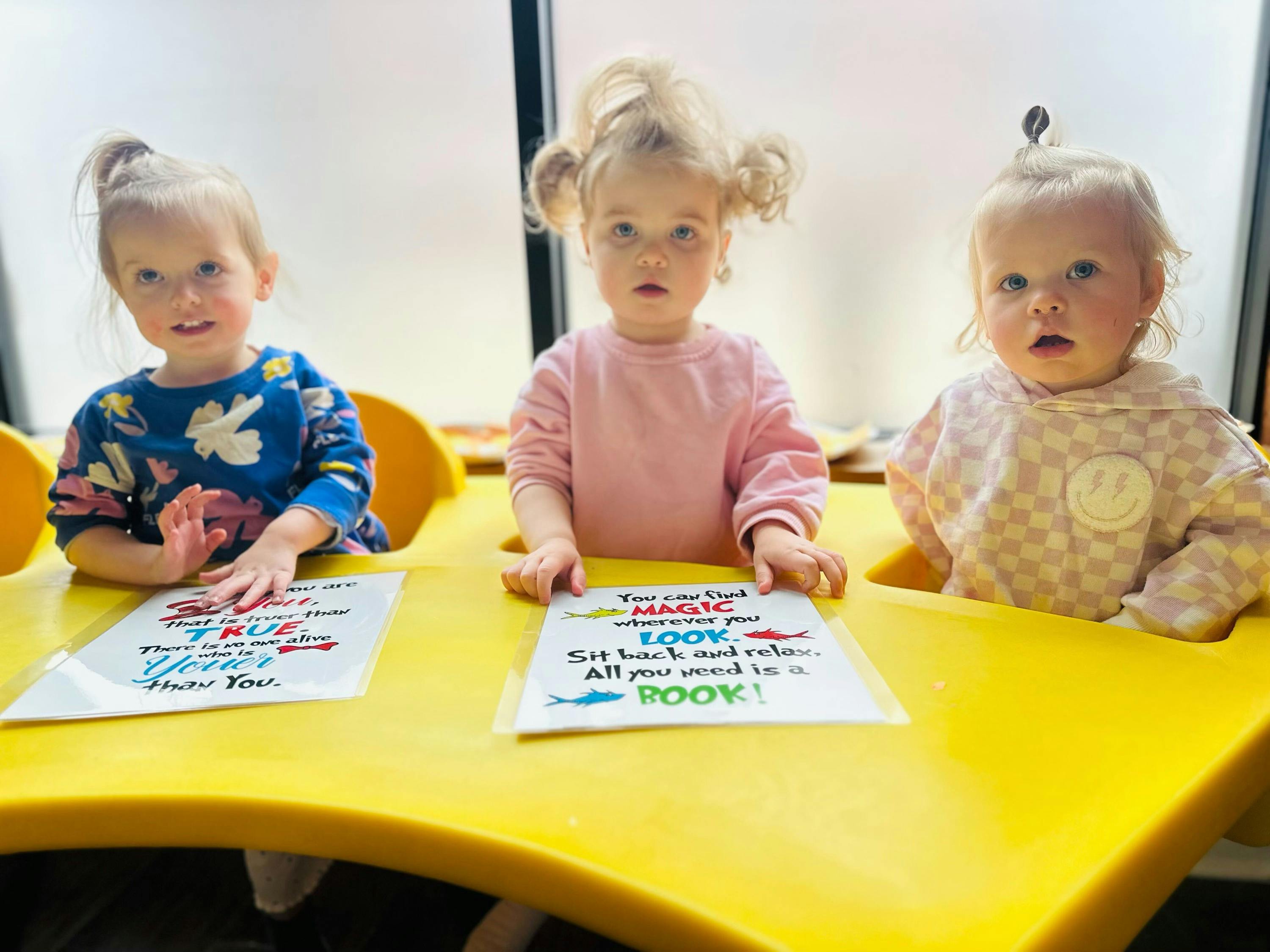 Three children sitting at a yellow table with papers in front of them papers with papers