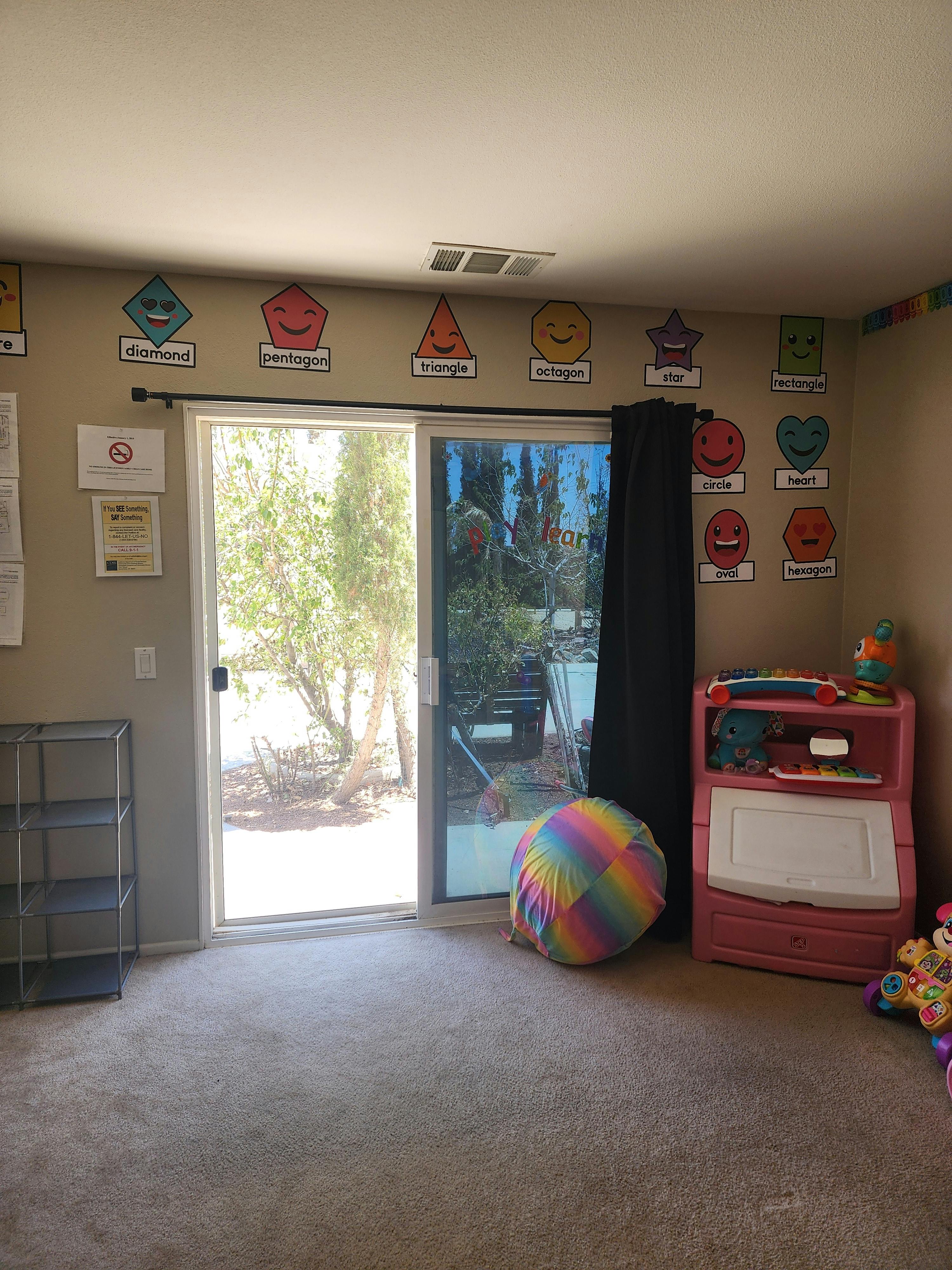 Room with sliding glass door, colorful shape cutouts on wall, and toy storage