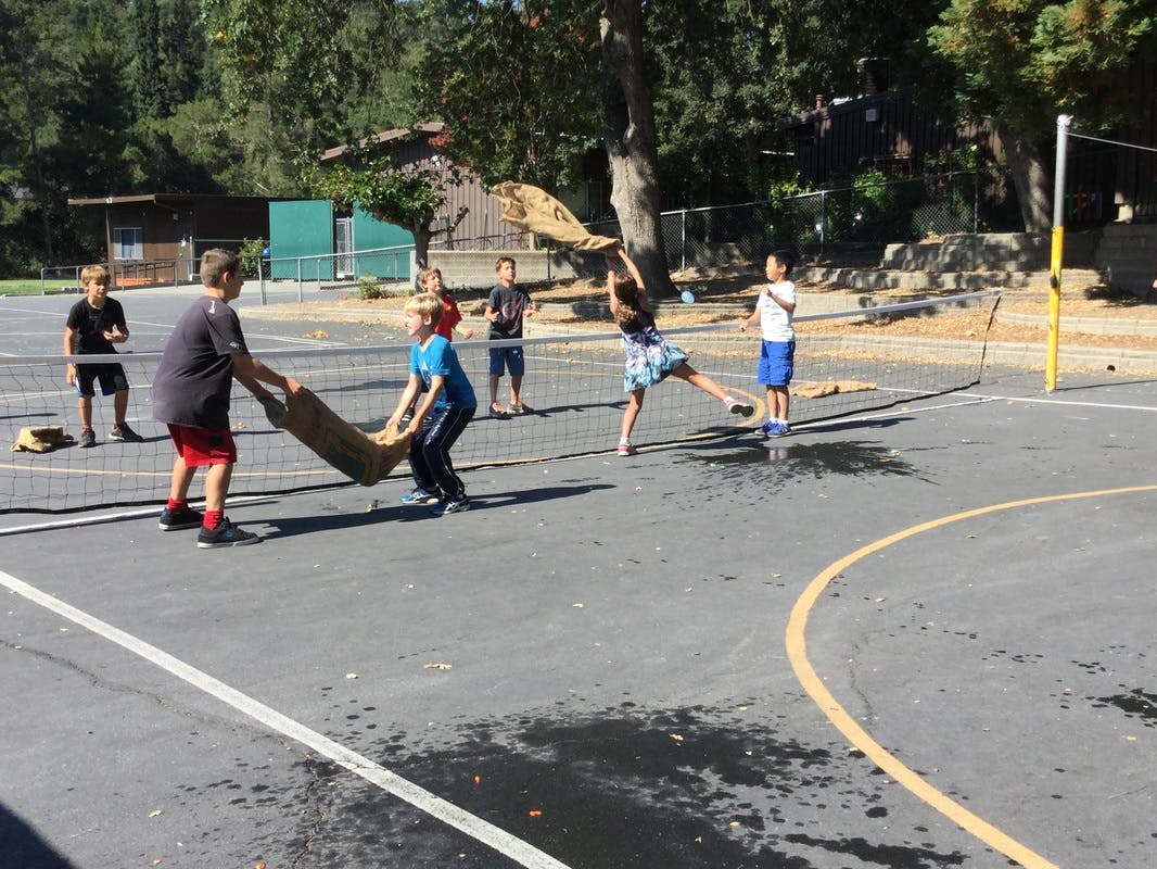 Children playing a game with a blanket on a paved court