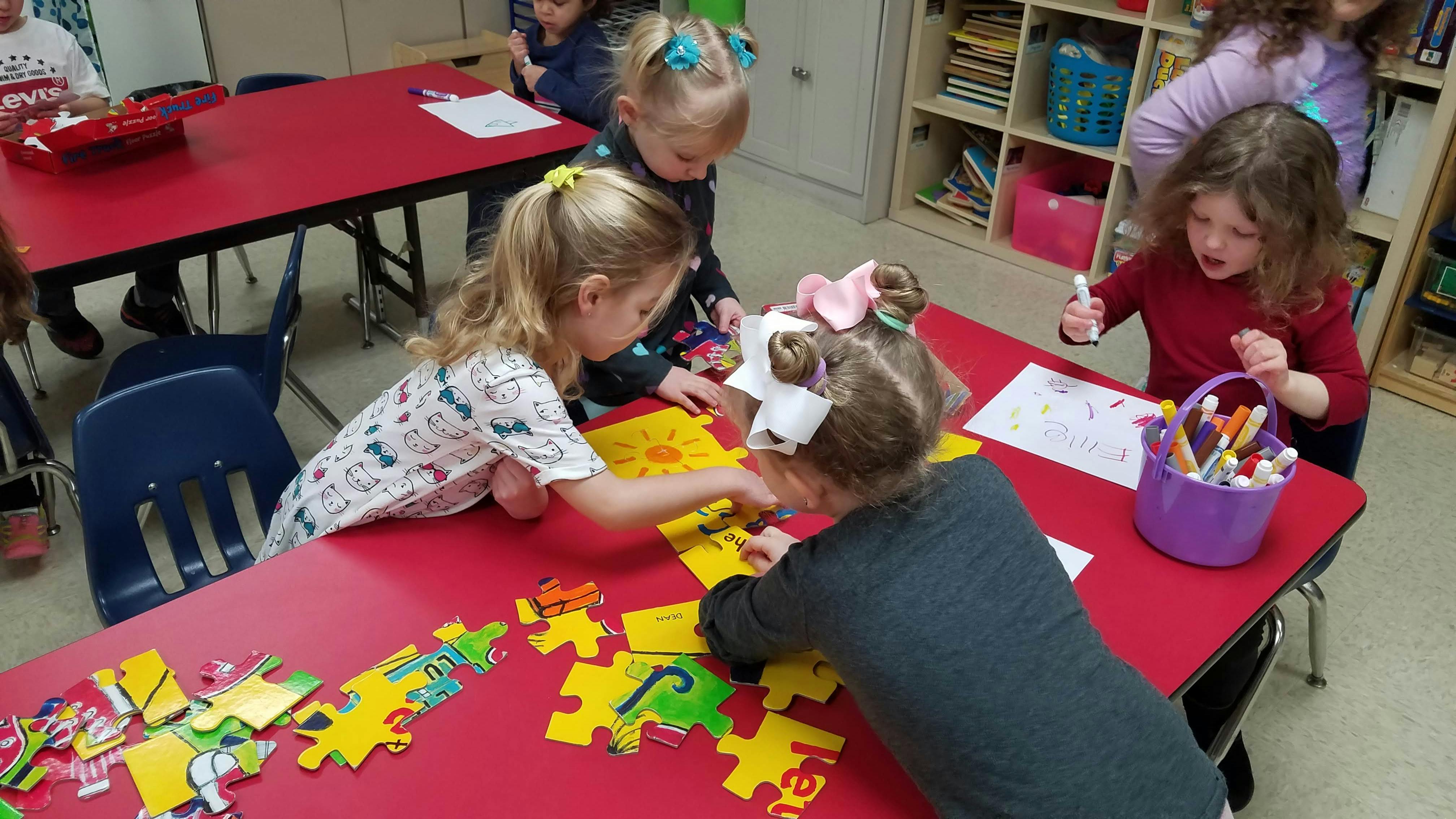 Children playing with puzzle pieces at a red table