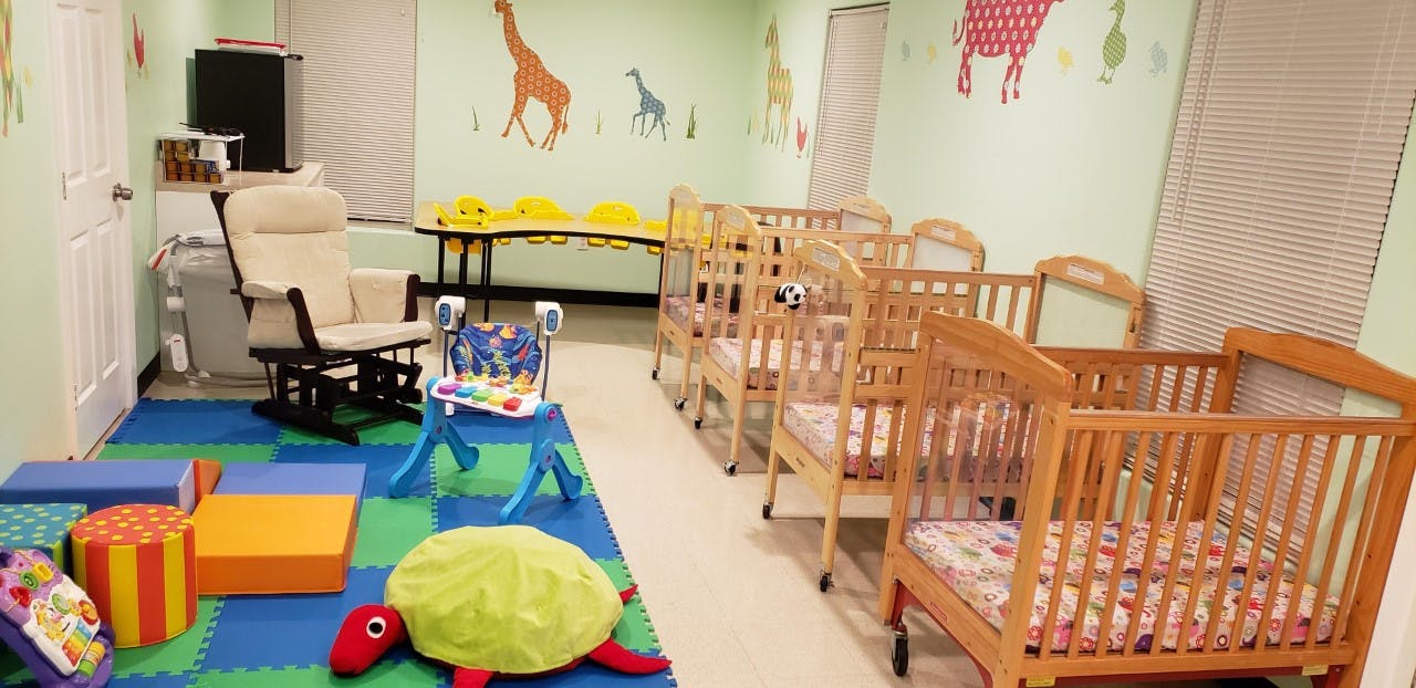 Nursery room with multiple cribs, a rocking chair, and play mats