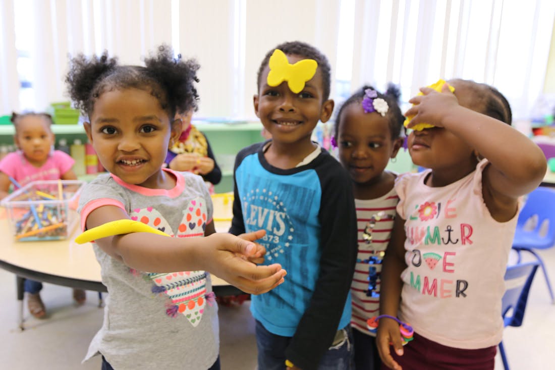 Four children playing with yellow butterfly cutouts in a classroom
