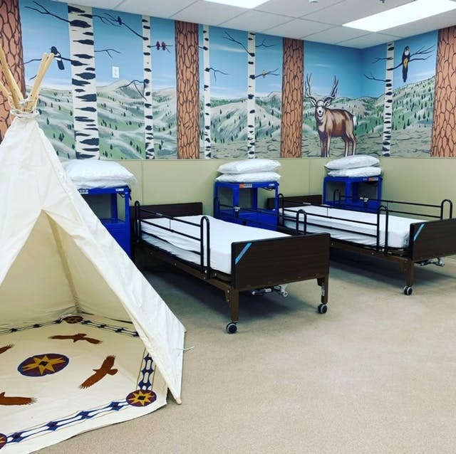Two hospital beds and a teepee in a room with a nature mural