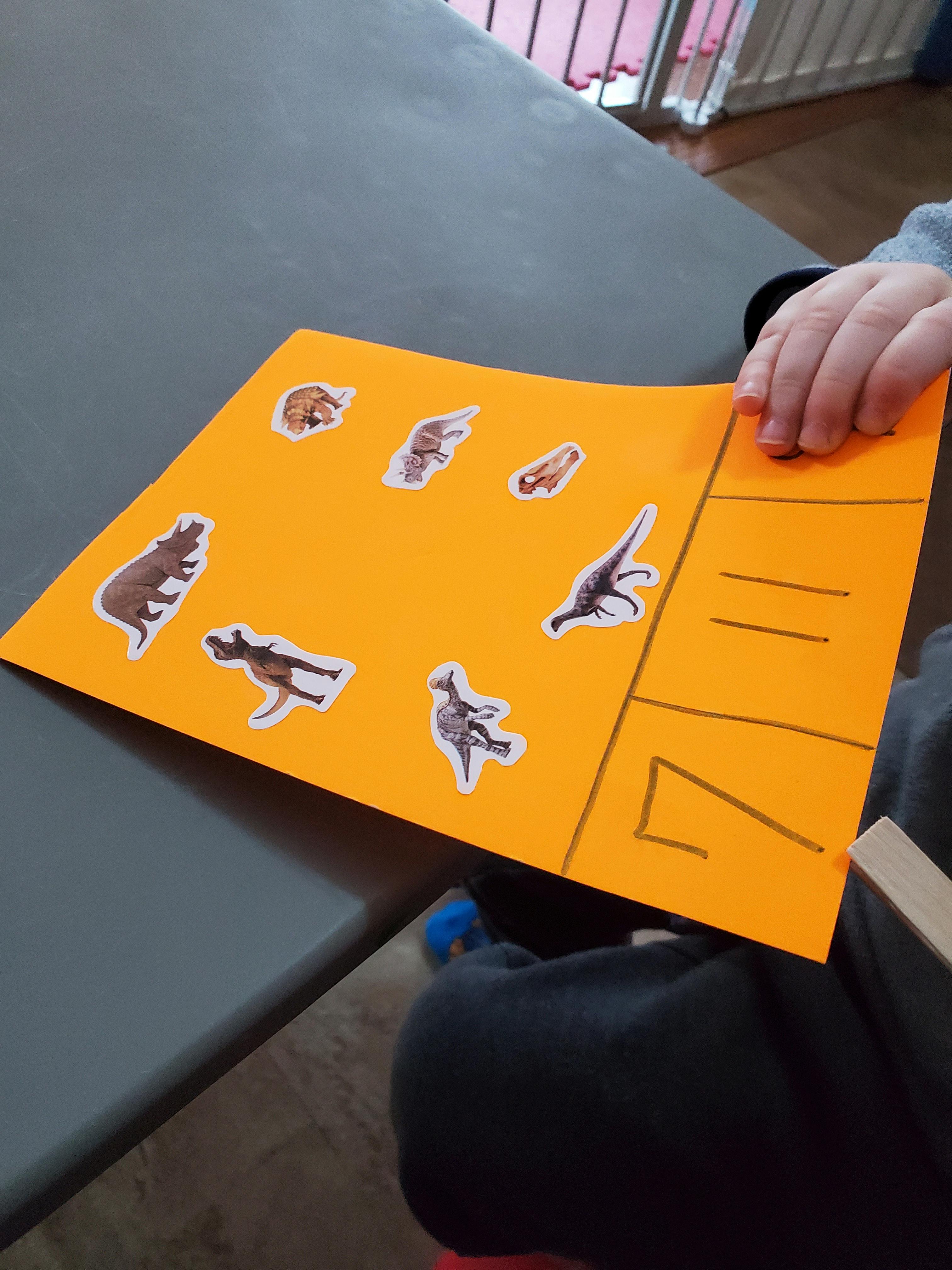 Child's hand holding orange paper with animal stickers and drawn lines